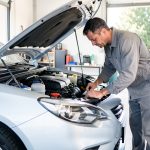 Entretien automobile quotidien : 8 gestes pour rouler sereinement Un homme vérifie les niveaux sous le capot et inspecte les pneus d’une voiture propre devant un garage lumineux.