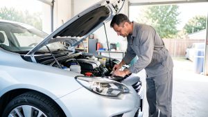 Un homme vérifie les niveaux sous le capot et inspecte les pneus d’une voiture propre devant un garage lumineux.